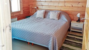 Une chambre dans une cabane en bois, avec un lit, une table de chevet et une fenêtre avec des stores.