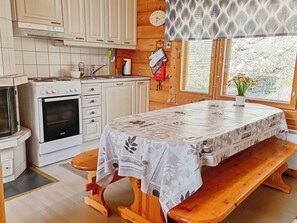 Een keuken met witte kastjes, een fornuis en een magnetron. Er staat een houten bank en een tafel met een tafelkleed.