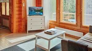 L’intérieur d’un chalet accueillant, avec des murs en bois, une table blanche, un canapé et un téléviseur posé sur une commode.