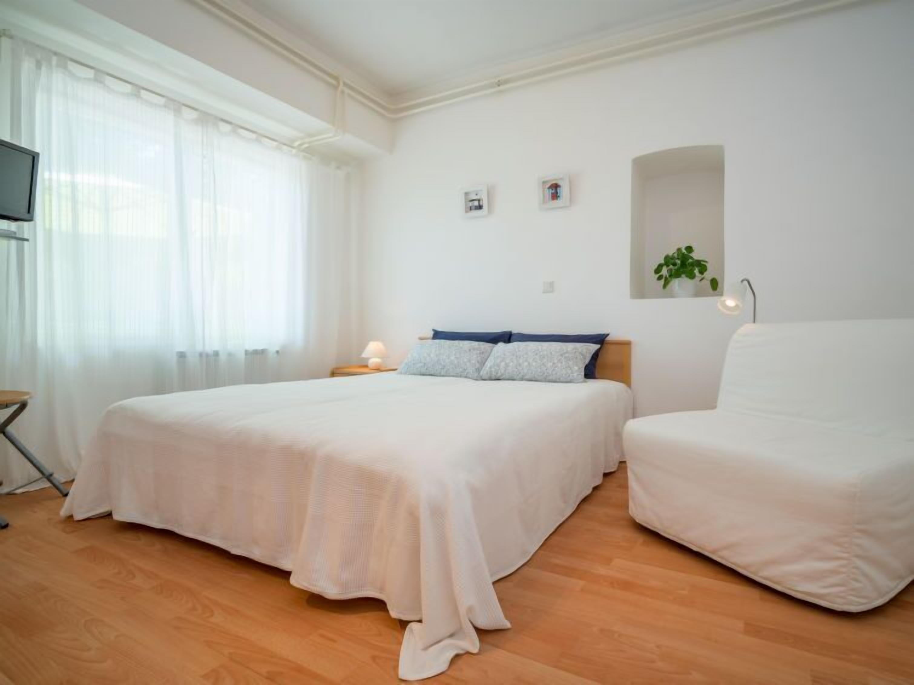 A bedroom with a large bed, a bedside table with a lamp, a chair, and a TV on a stand.