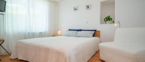 A bedroom with a large bed, a bedside table with a lamp, a chair, and a TV on a stand.