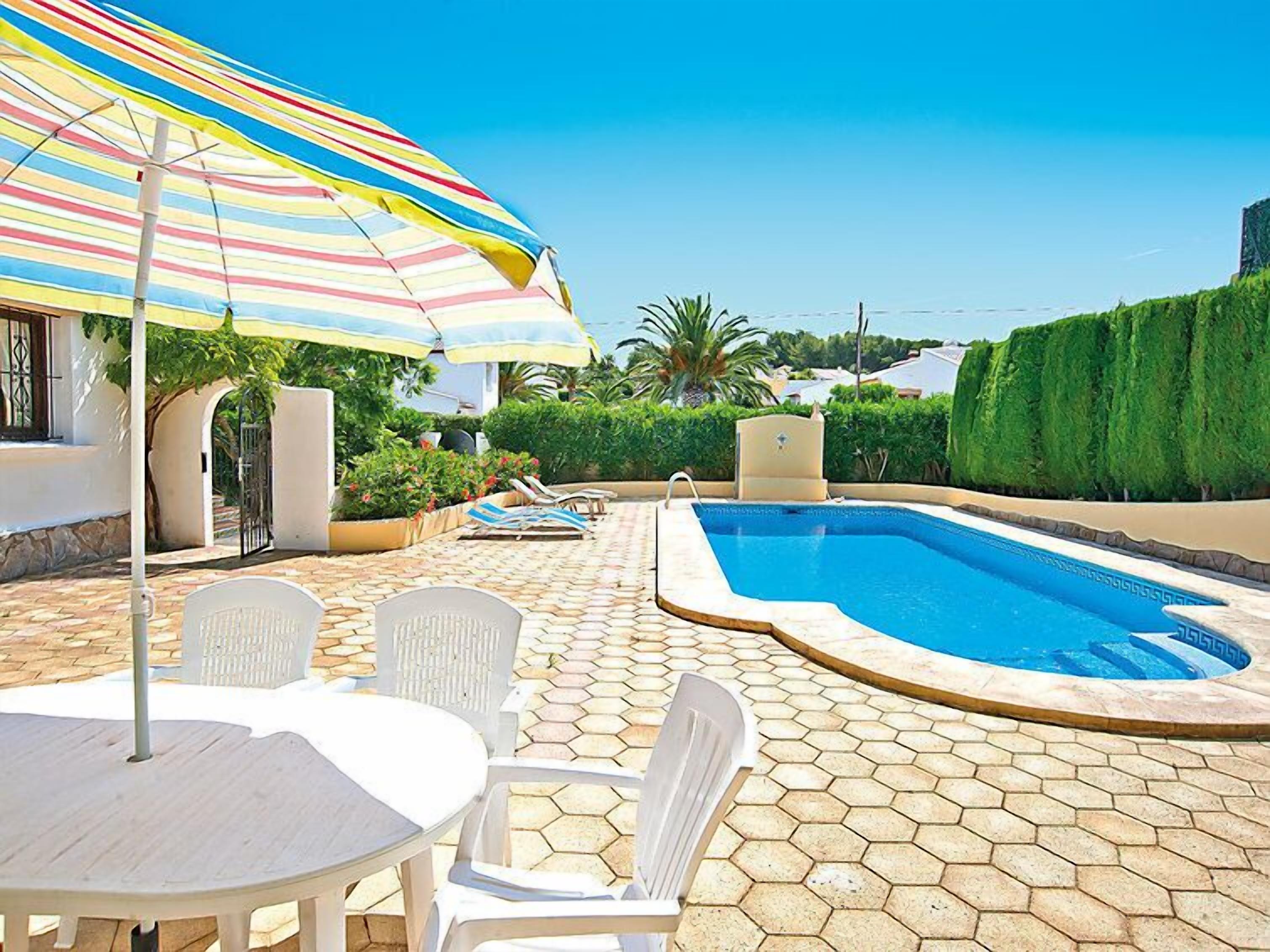 A swimming pool with a hexagonal tiled deck, surrounded by white lounge chairs and a table.
