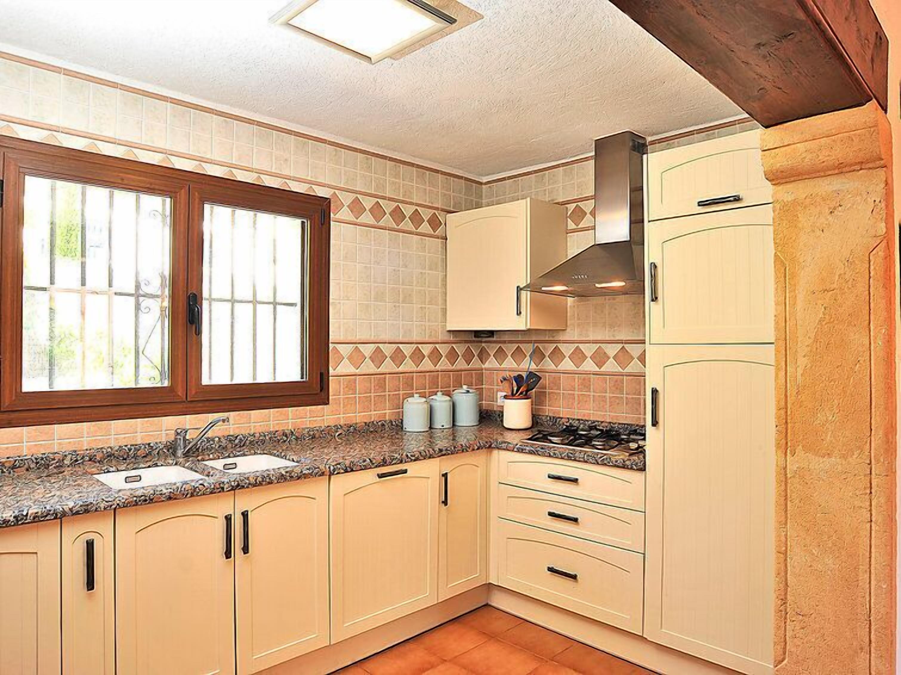 Una cocina con armarios color crema, un ventanal con vistas, estufa y salpicadero de azulejos.