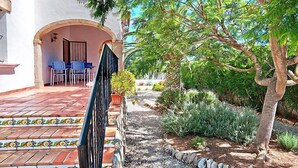 A patio with a tiled floor, a black metal gate, and a small garden with various plants and a tree. - Rocinante by Interhome (Jávea)