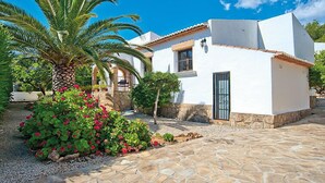 A white building with a stone-paved courtyard, a palm tree, and red flowers. - Rocinante by Interhome (Jávea)