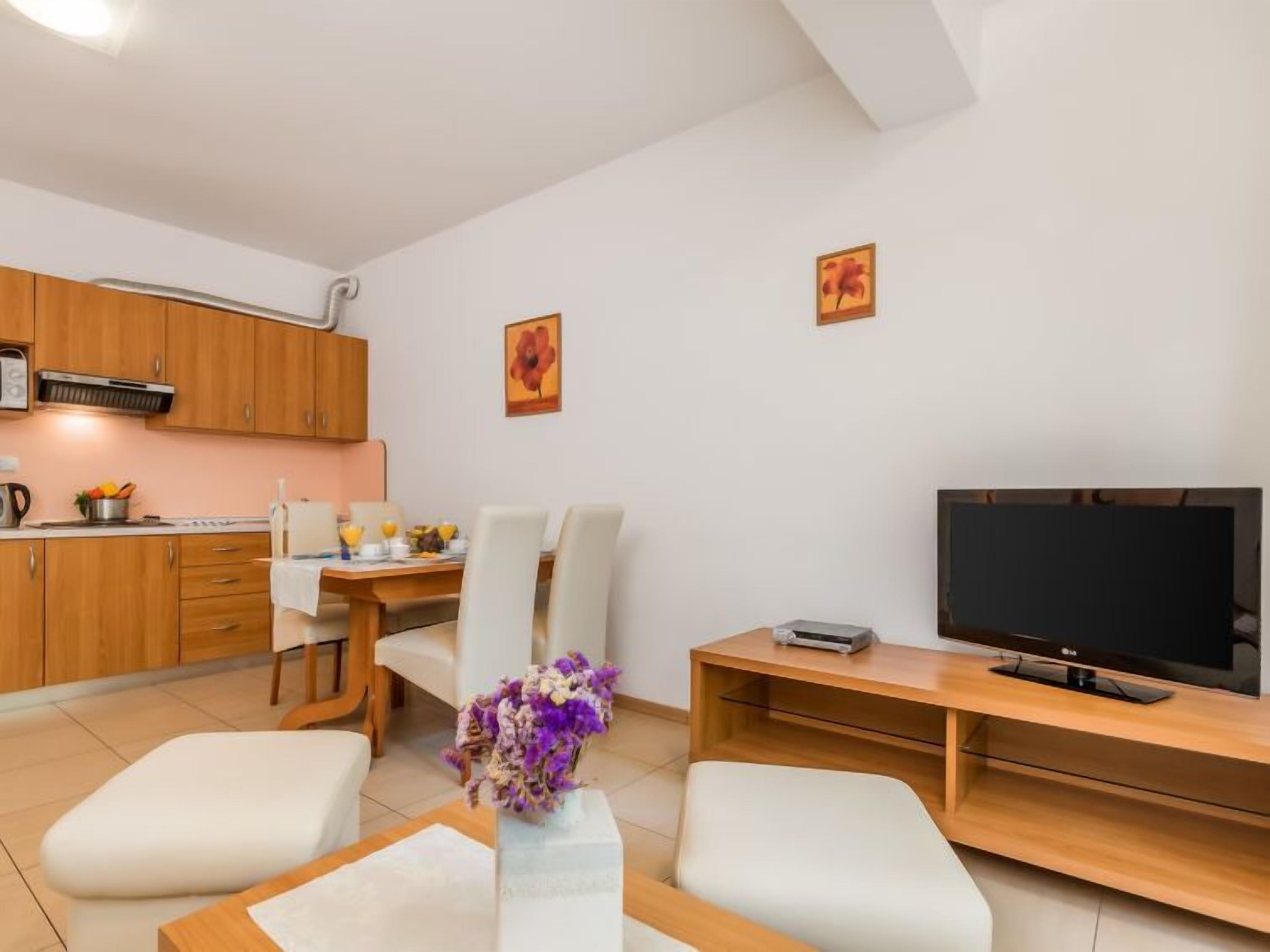 Uma sala de estar moderna com televisão de tela plana, mobiliário de madeira e um espaço de jantar com mesa e cadeiras.