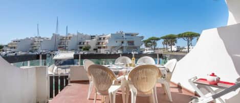 A terrace with a table and chairs, overlooking a marina with boats and buildings.