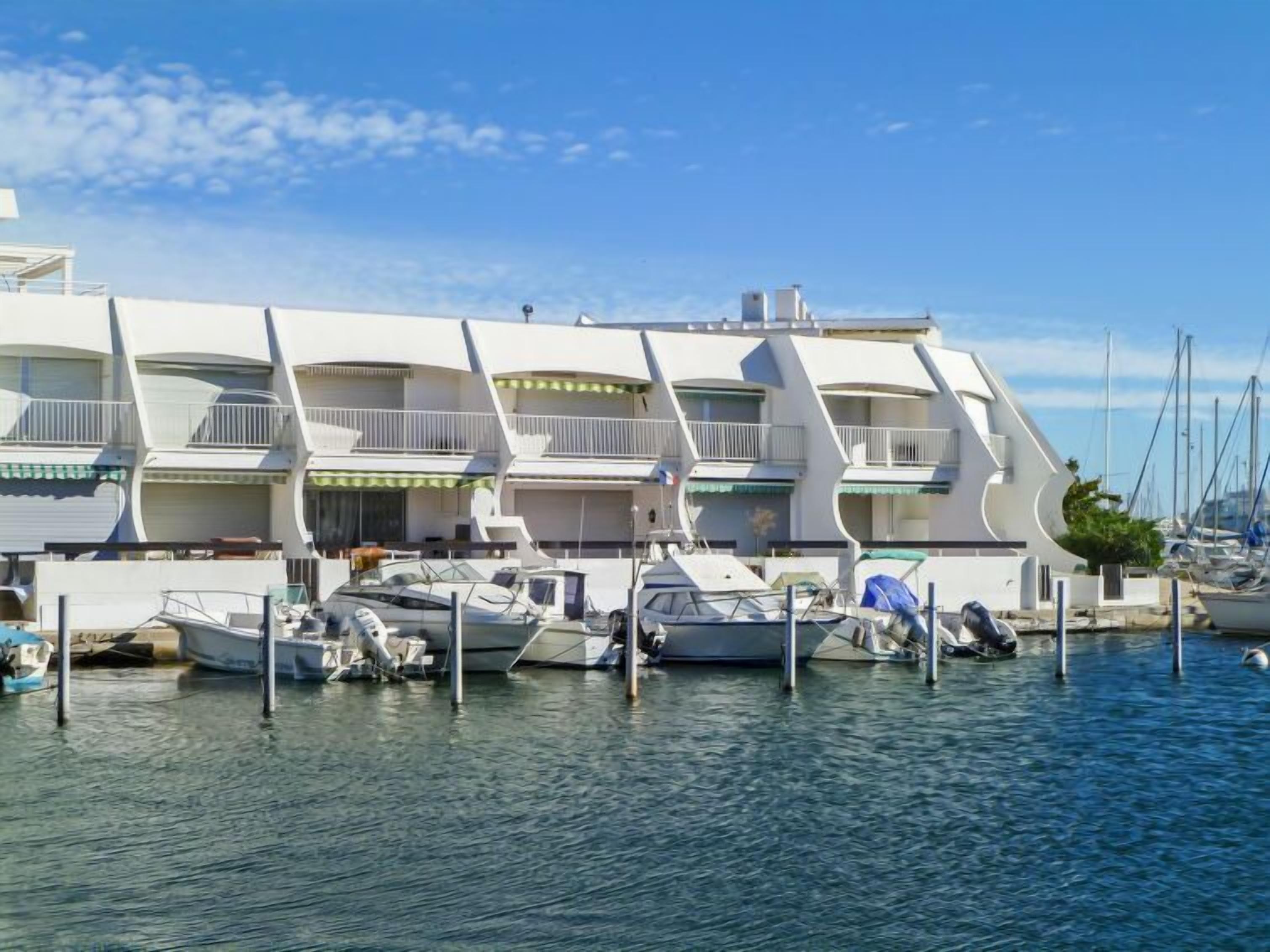 Una marina moderna con un design architettonico distintivo, caratterizzata da numerosi balconi e da una serie di imbarcazioni ormeggiate.