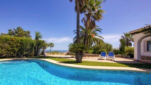 Ein klarer, blauer Swimmingpool mit zwei Liegestühlen, umgeben von Palmen und Blick auf den Ozean.