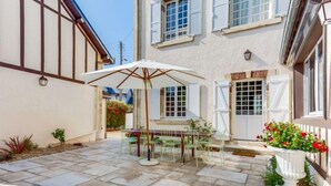 A courtyard with stone flooring, a table with chairs, and a white umbrella. - Le Cyclamen by Interhome (Courseulles)