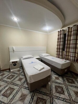 A hotel room with two beds, a nightstand, a small table, and a patterned floor. - Hotel City II (Santo André)