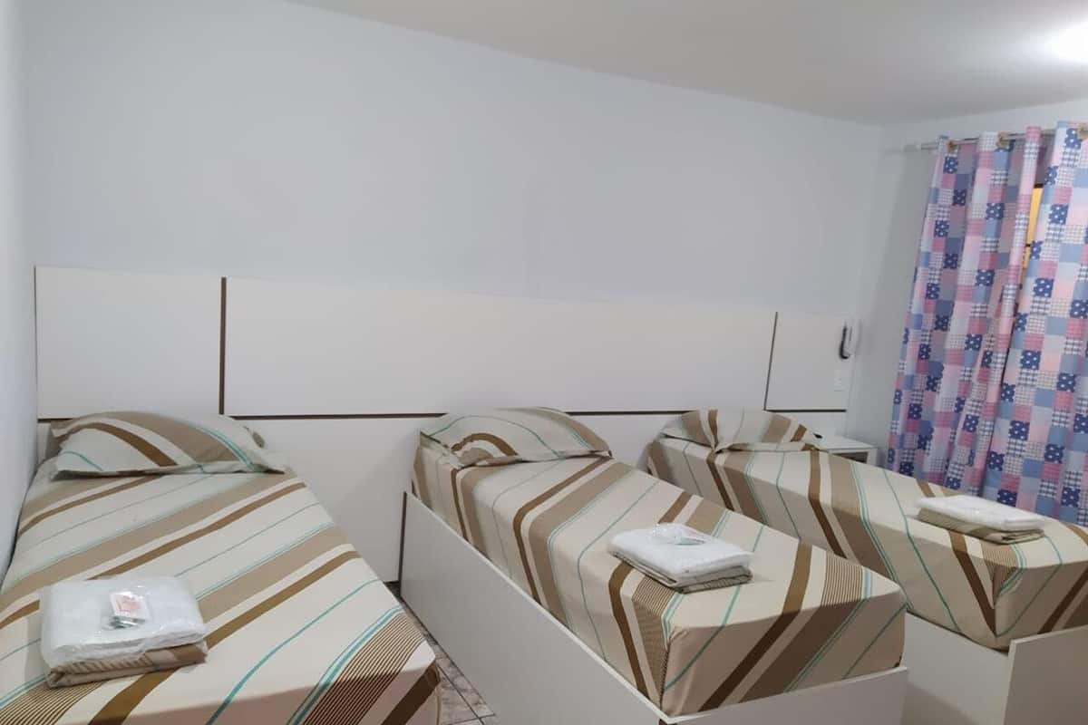 Une chambre d’hôtel avec trois lits simples, chacun doté de draps à rayures et d’un oreiller blanc.
