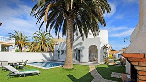 Ein modernes Haus mit Swimmingpool, einer Terrasse mit Liegestühlen und einem gepflegten Rasen.