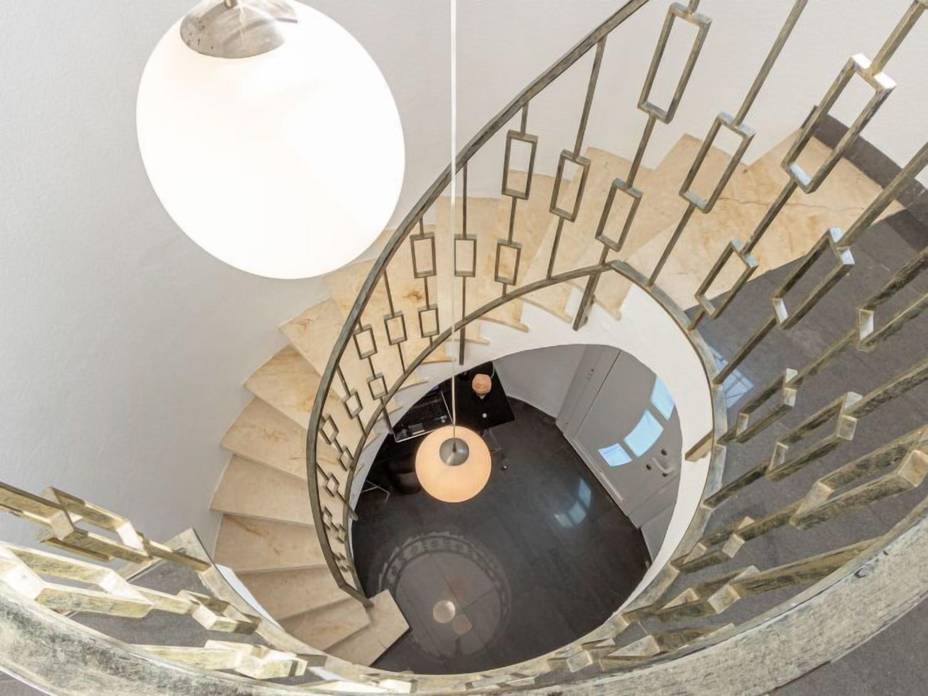 A spiral staircase with a geometric metal railing and a hanging light fixture.