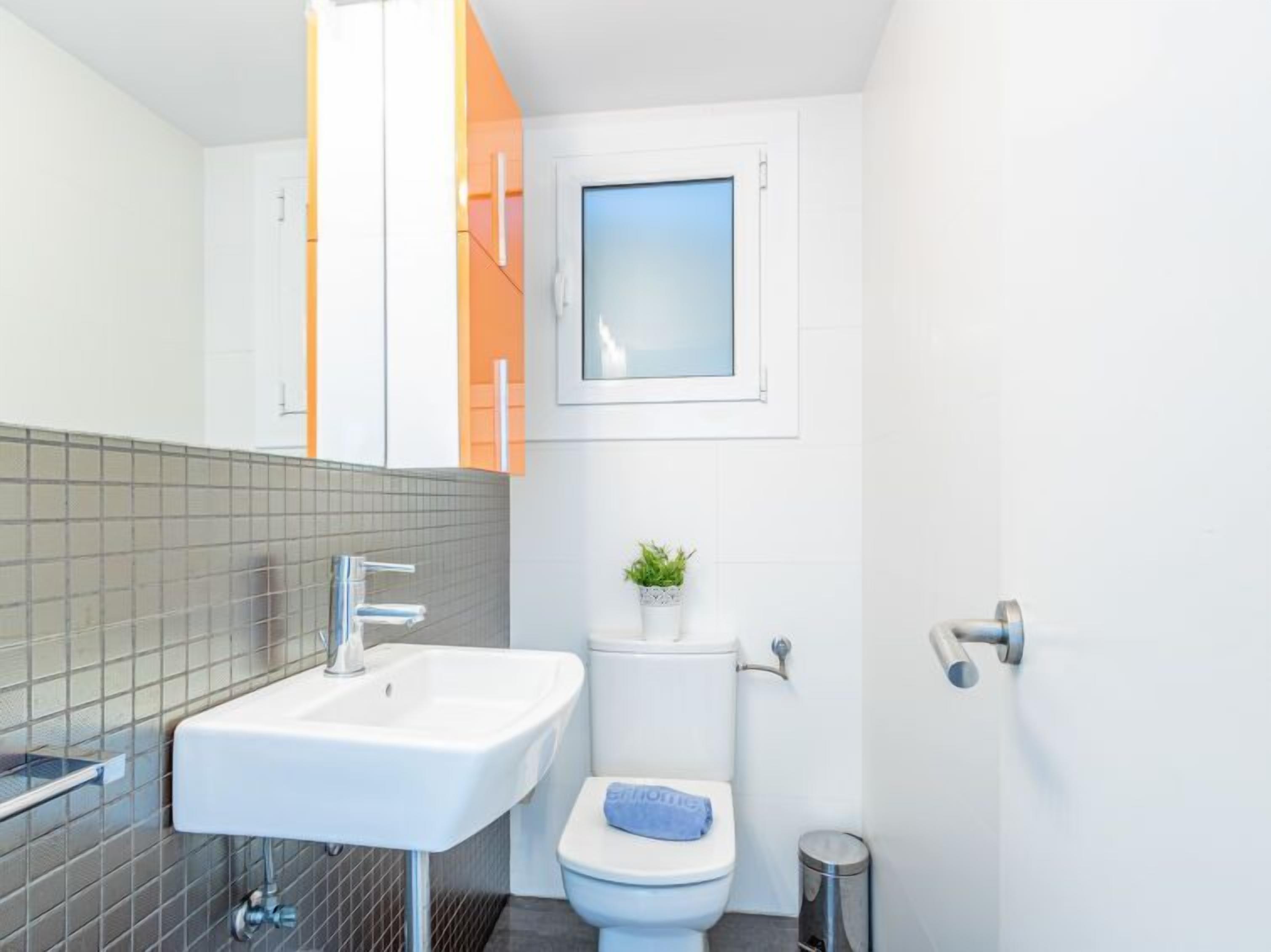 Ein modernes Badezimmer mit einem weißen Waschbecken, einer Toilette und einem kleinen Fenster.