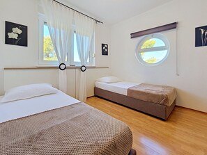 A hotel room with two beds, a window with curtains, and a small round window. - Apartment Anđa by Interhome (Trogir/Slatine)