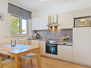 A modern kitchen with a dining area, stainless steel appliances, and a window with a view of trees. - Apartment Anđa by Interhome (Trogir/Slatine)