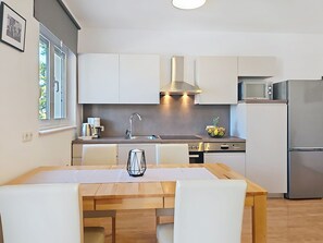 Et moderne køkken med hvide skabe, et rustfrit stål køleskab og et spisebord med stole.