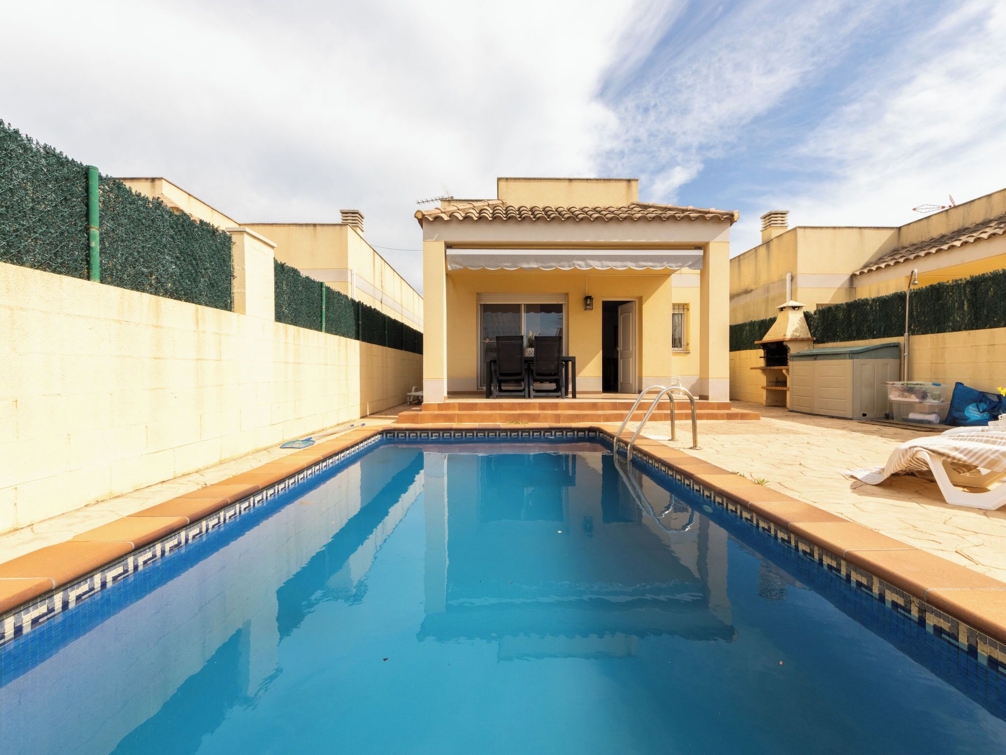 A swimming pool with a patio area, a covered seating area, and a barbecue grill.
