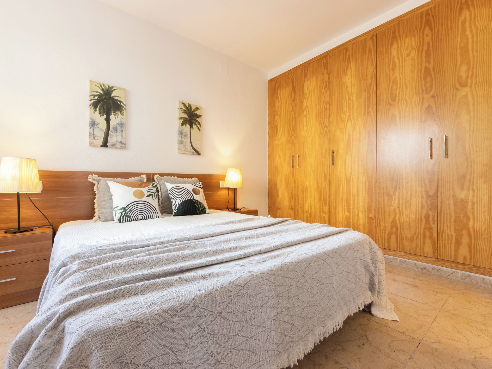 Quarto com uma cama grande, duas luminárias fixadas na parede e um guarda-roupa de madeira.