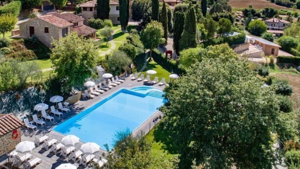 A pool area with lounge chairs and umbrellas, surrounded by greenery and buildings. - Casa Graziani by Interhome (Città della Pieve)