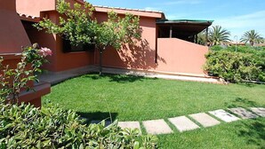 A building with a red exterior, a green lawn, and a stone pathway. - Marrone by Interhome (Costa Rei)