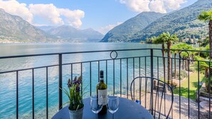 A table with a bottle of wine and two glasses, overlooking a lake with mountains in the background.