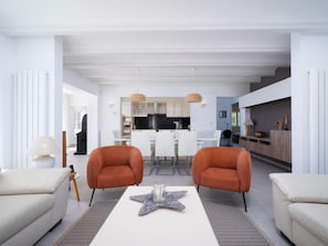 A modern living room with two orange armchairs, a white coffee table with a star decoration, and a kitchen in the background.