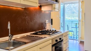 Une cuisine moderne équipée d’une cuisinière à gaz, d’un évier et d’un four, ainsi qu’une grande fenêtre donnant sur un balcon.