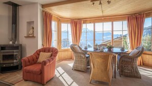 Una habitación acogedora con chimenea, una mesa de comedor con sillas y grandes ventanales con vistas a la montaña.