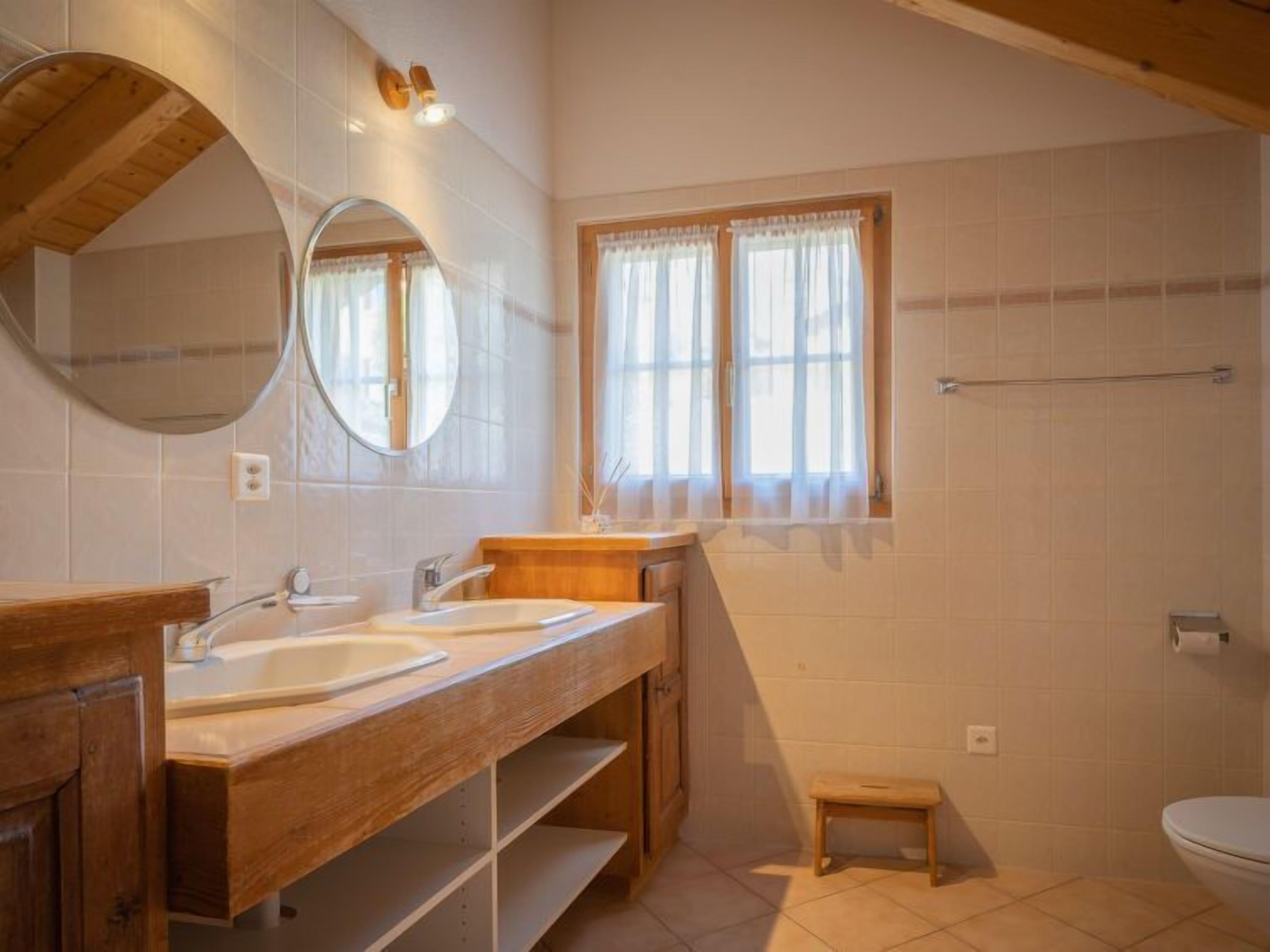 Un baño con dos lavamanos, un espejo, una ventana con cortinas y un mueble de tocador de madera.