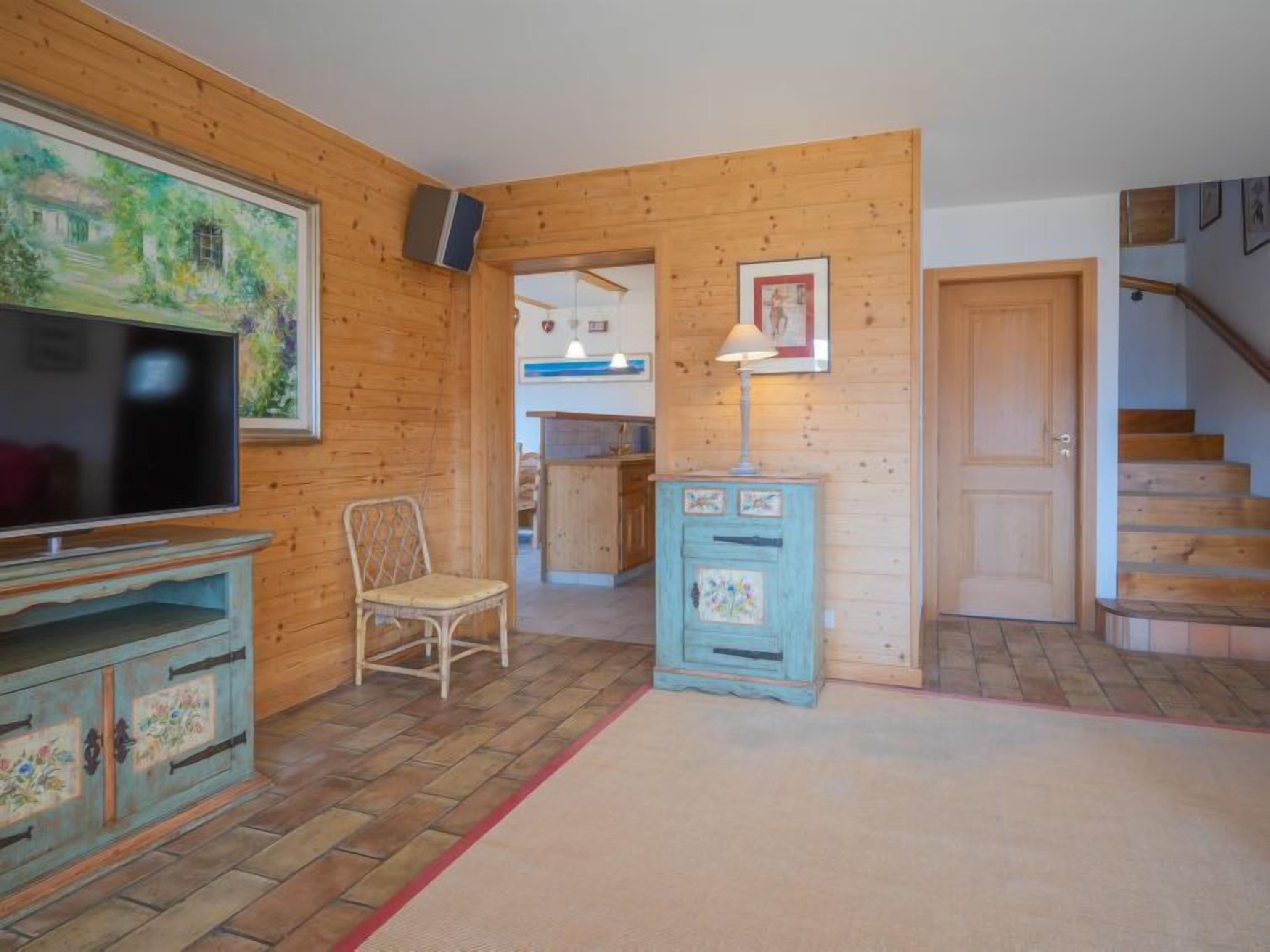 A wooden-paneled room with a television, a chair, a cabinet, and a staircase.