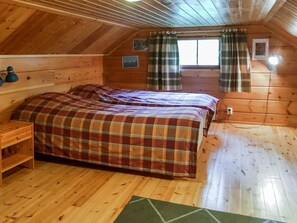 Un dormitorio acogedor en el ático con piso de madera, colcha a cuadros y ventana con cortinas.