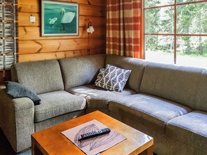 A corner sofa with a remote control on a table, a wall-mounted lamp, and a painting of swans. - Lomamaja rukaranta 6 b by Interhome (Kuusamo)