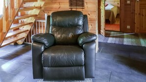 A black leather recliner in a wooden cabin with a wooden staircase and a door leading to another room.