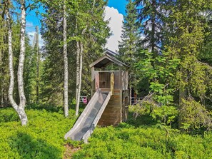 Une cabane en bois avec un toboggan en bois, située dans une zone boisée.