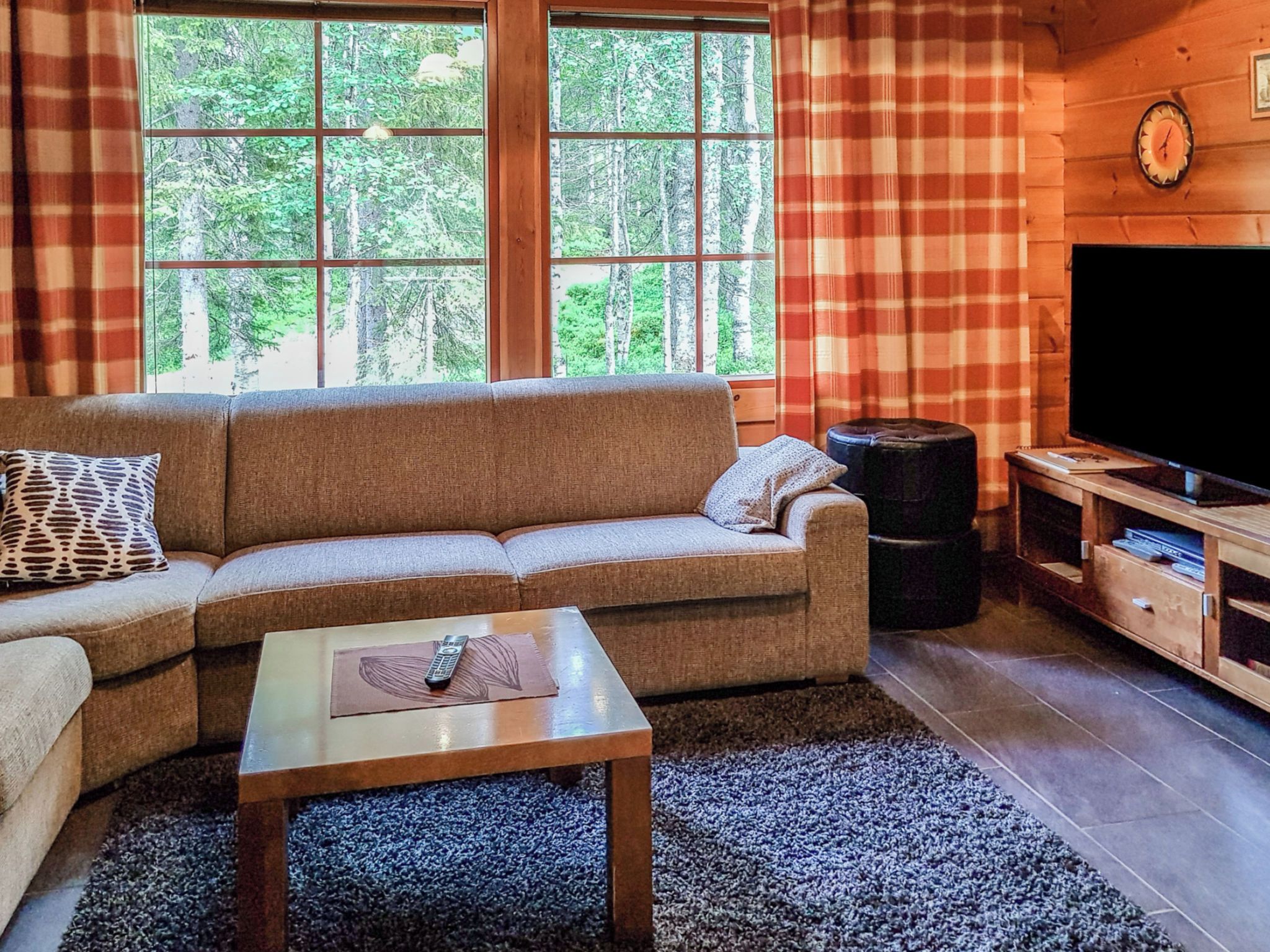 Uma sala de estar aconchegante com sofá, mesa de centro, televisão e janela com vista para árvores.