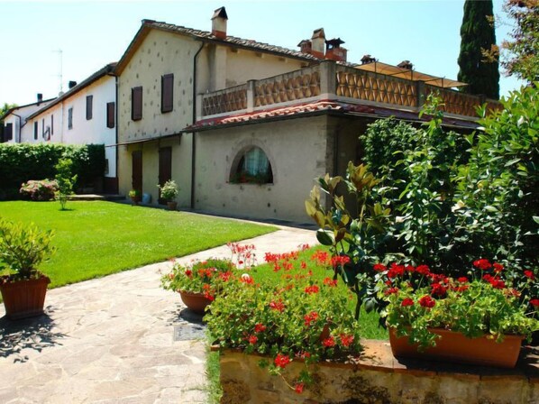 A traditional building with a tiled roof, a stone pathway, and potted plants with red flowers.