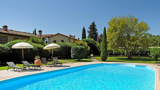 Ein Swimmingpool mit Liegestühlen und Sonnenschirmen, umgeben von gepflegten Hecken und blauem Himmel.