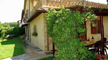 Un edificio in pietra dalle linee classiche, con un portico coperto e un giardino rigoglioso.
