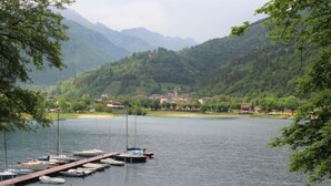 Un lago con barche ormeggiate a un molo, circondato da colline verdeggianti e un piccolo villaggio sullo sfondo.