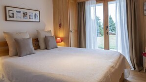 A bedroom with a large bed, a wooden wardrobe, a door leading to a balcony, and a framed picture on the wall.