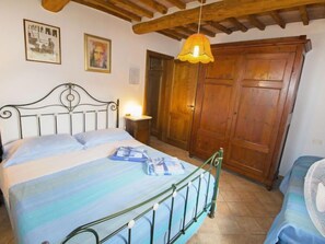 Une chambre à coucher comprenant un lit, une armoire en bois, une table de chevet avec une lampe et un luminaire suspendu.