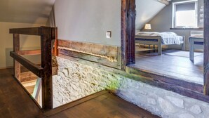 Un dormitorio estilo loft con vigas de madera a la vista, una pared de piedra y un amplio ventanal de arco.