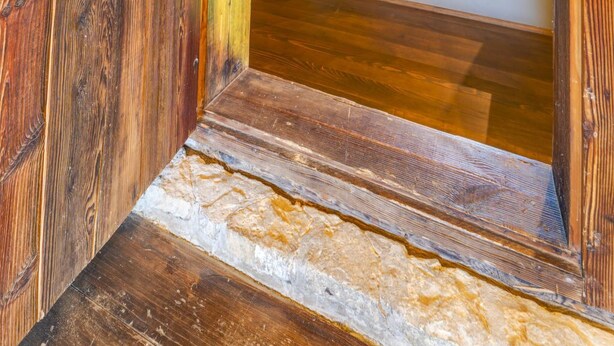 Una escalera de madera conduce a un pasillo en el segundo piso, con un marco de puerta de madera y un espejo.