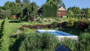 Una cabaña de madera con techo inclinado, rodeada por un jardín cuidado y una piscina.