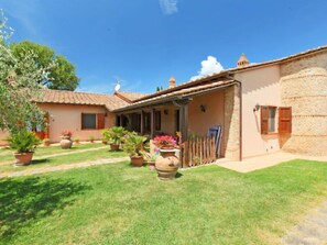 A two-story house with a tiled roof, a stone wall, and a covered patio area.