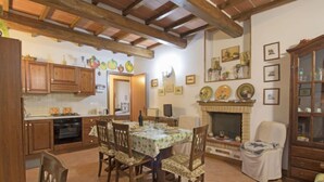 A cozy kitchen with wooden cabinets, a dining table with chairs, a fireplace, and various framed pictures on the wall.