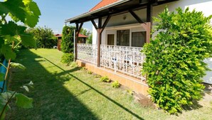 Ein Haus mit rotem Ziegeldach, einer überdachten Veranda mit weißer Brüstung und einem gepflegten Garten.