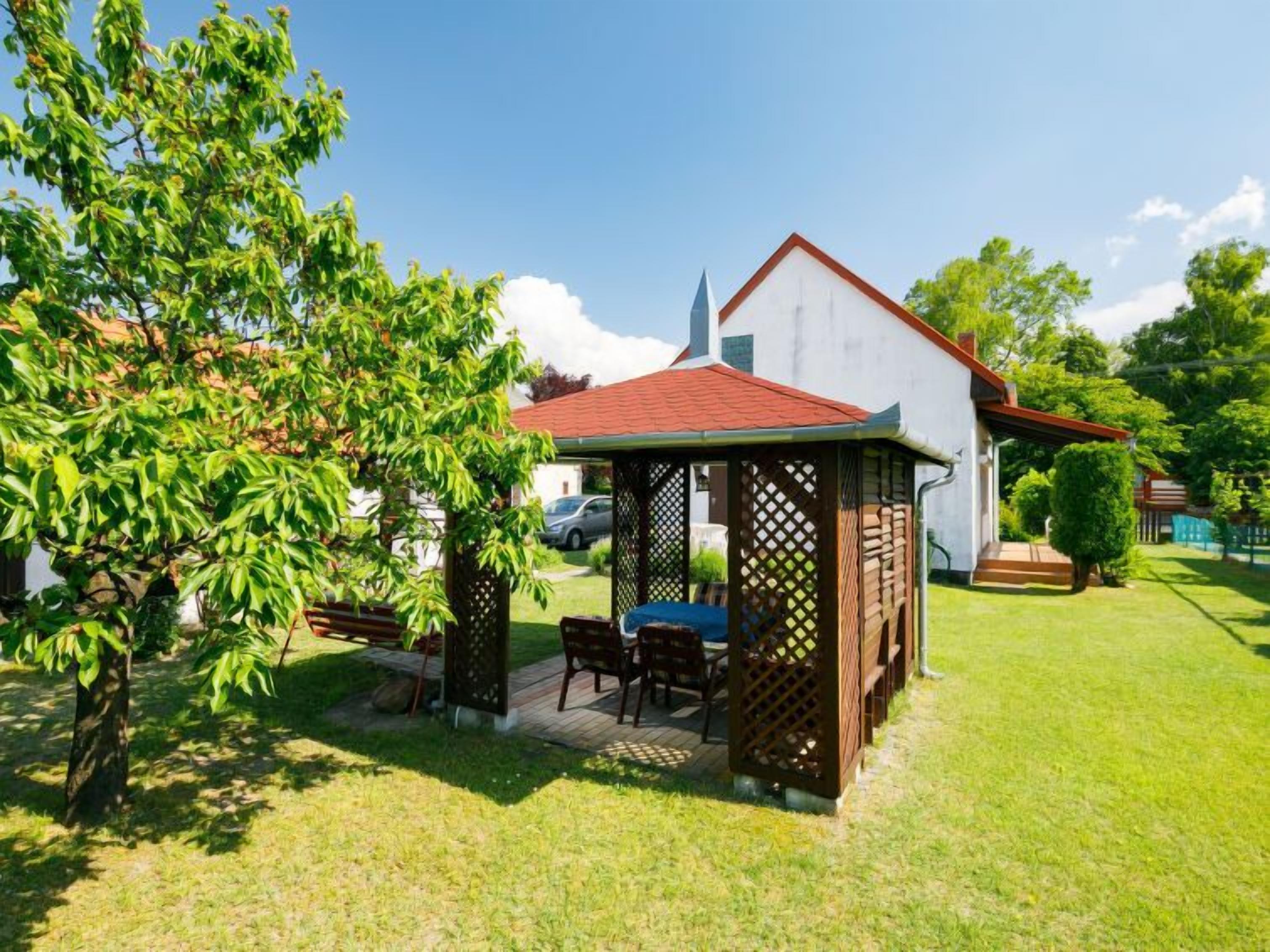 A gazebo with a table and chairs, surrounded by a well-maintained lawn and trees.